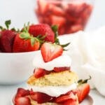 Easy homemade strawberry shortcake recipe on small white plates with bowl of strawberries in the background.