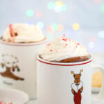 Peppermint hot chocolate in reindeer mugs with colored lights in the background.