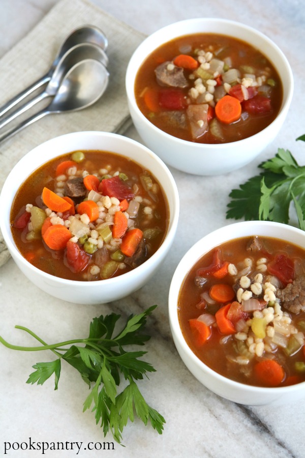 3 bowls of beef barley soup with parsley and spoons
