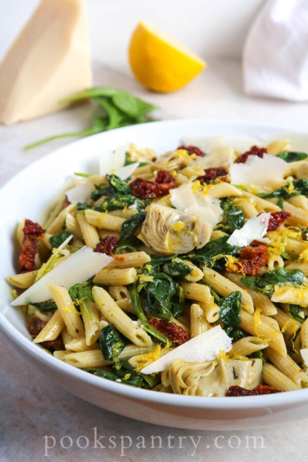 Bowl of penne pasta with lemon, spinach and artichokes.