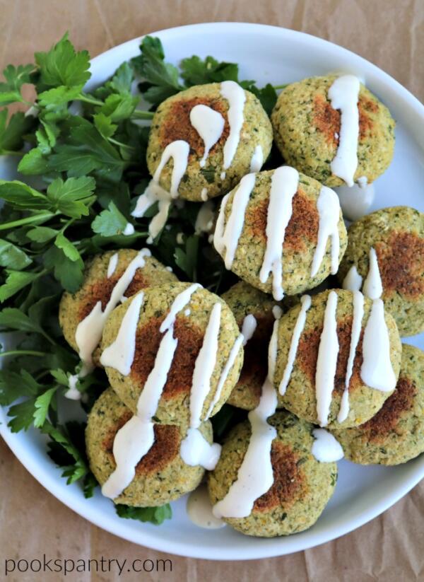 baked falafel stacked on white plate with drizzle of tahini sauce