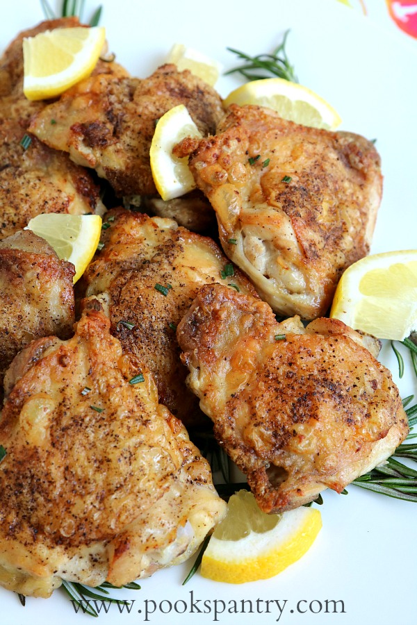 crispy chicken thighs on platter with lemon and rosemary