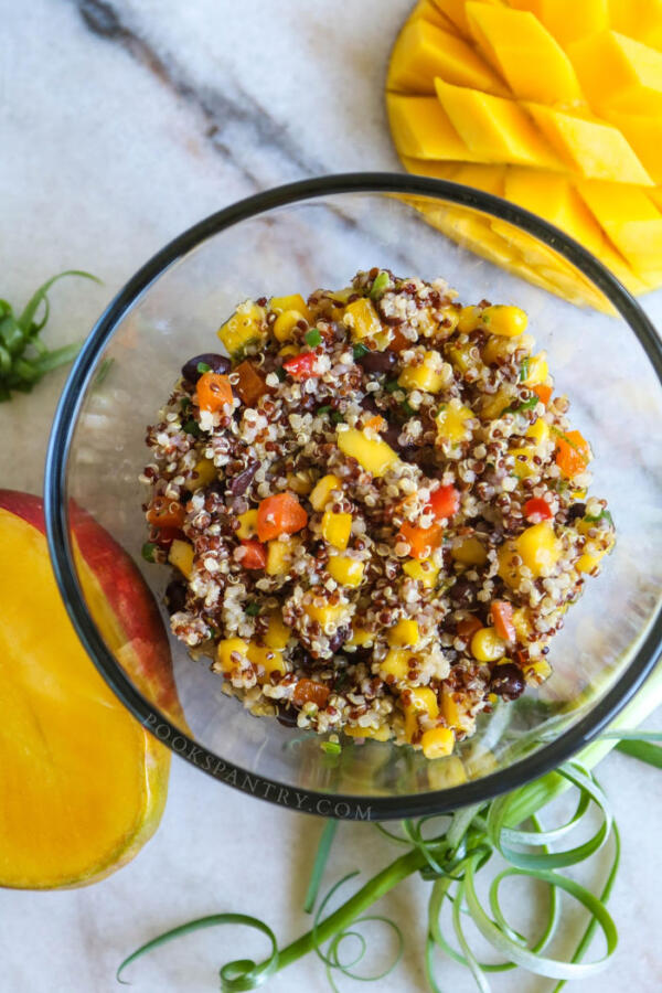 Quinoa salad with black beans and mango in glass bowl with curly scallions.