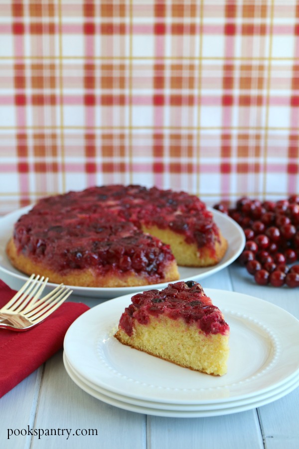 slice of cranberry upside down cake on stacked white plates with cake in background