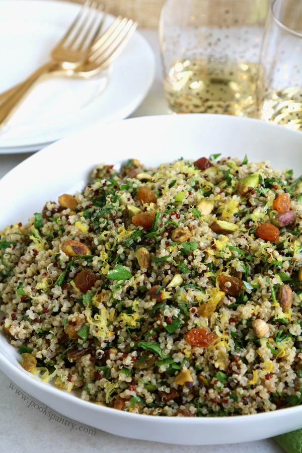 mediterranean quinoa salad in shallow white bowl with gold forks and wine glass in background