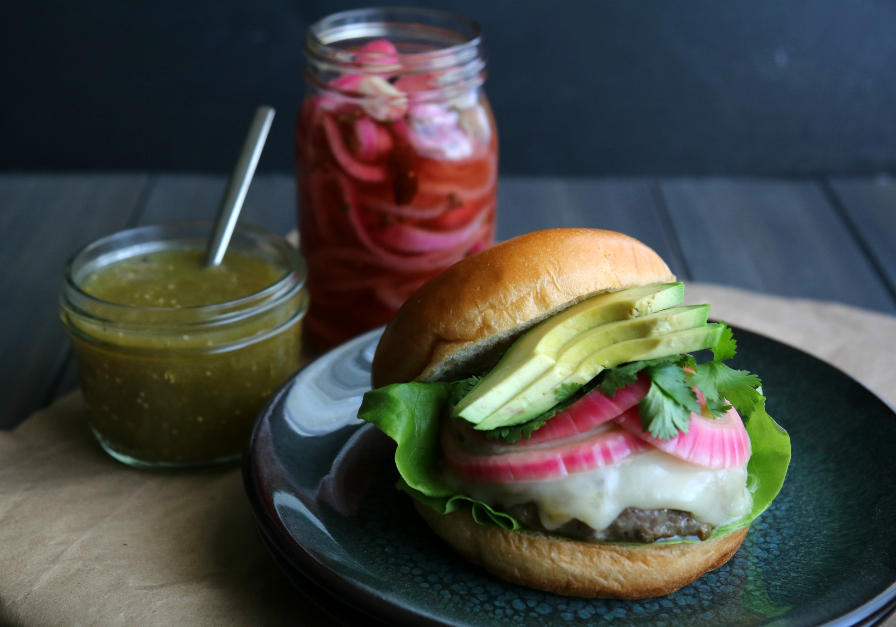 Hatch Chile Pork Burger on plate with green salsa and pickled onion