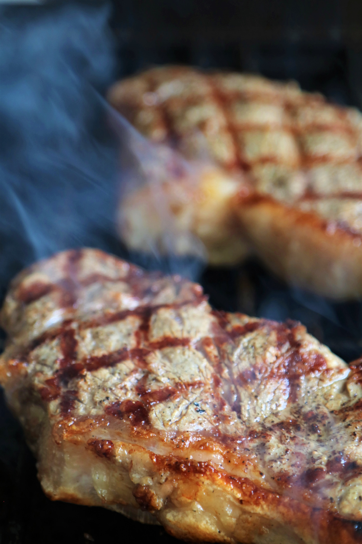 Smoke coming off of steaks on a grill.