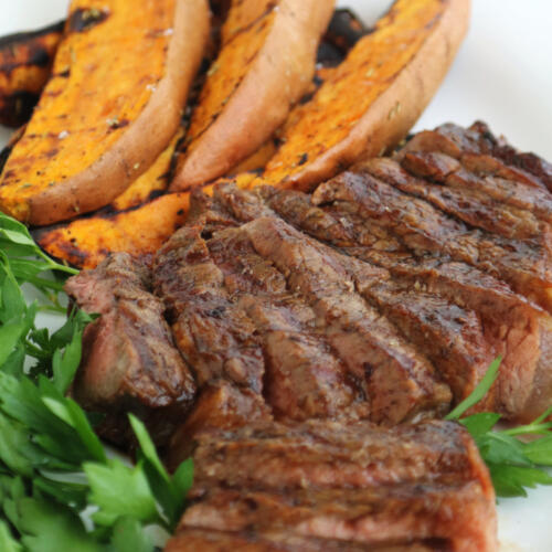 Espresso bourbon steak sliced on a platter with grilled sweet potatoes.