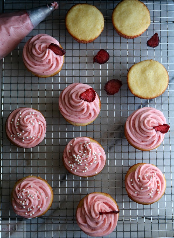 Vanilla Cupcakes with Strawberry Cream Cheese Frosting and sprinkles on a cooling rack.