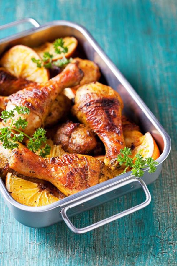 chicken legs and oranges in casserole dish with teal background