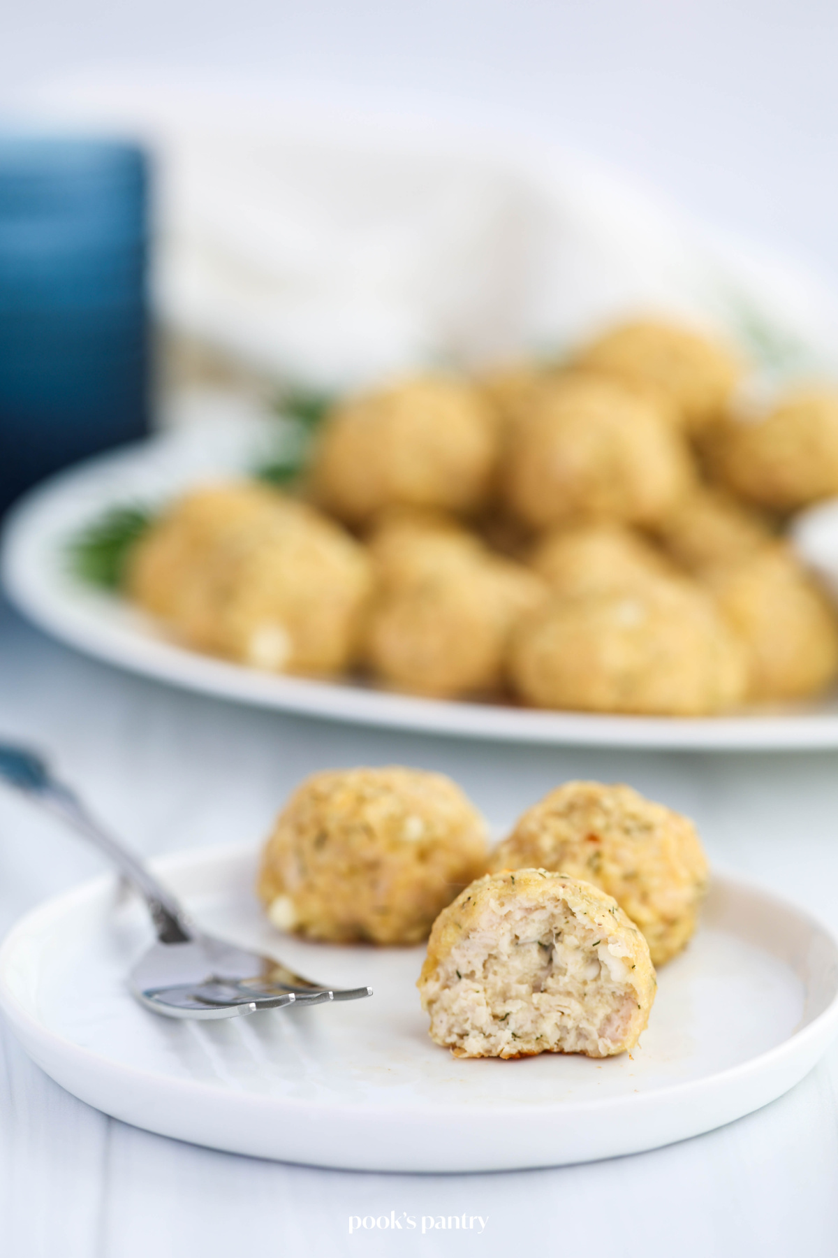 Three meatballs on a small white plate, with a silver fork. One of the meatballs is cut open to show the inside.