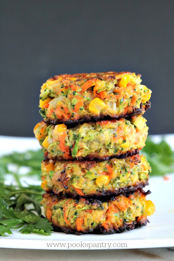Stacked veggie cakes with herbs on white platter with black background.