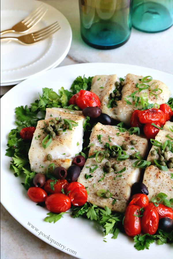 baked corvina on white platter with tomatoes and olives