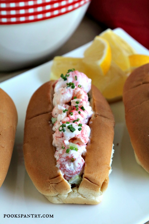 lobster roll on plate with red and white check bowl in background