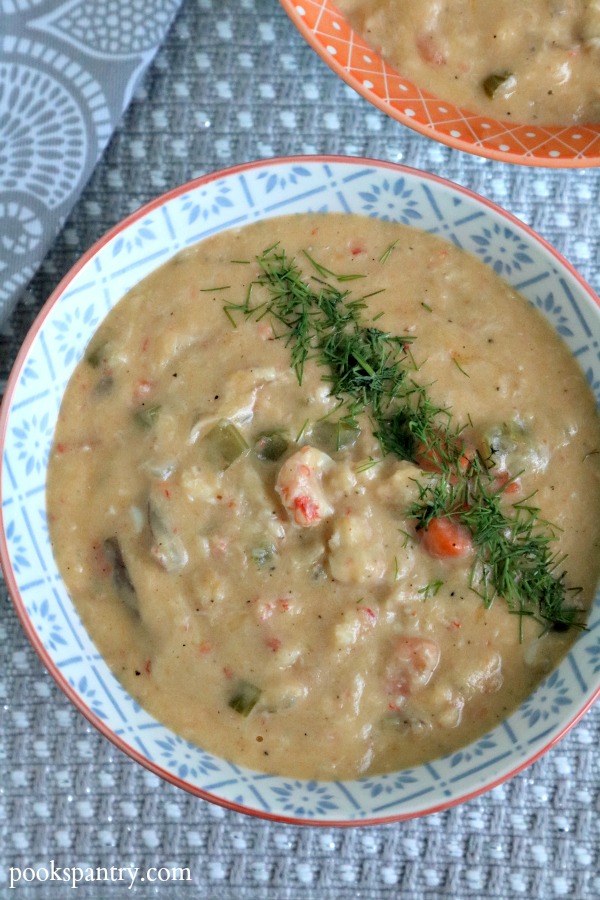 bowl of langostino chowder with dill garnish on gray placemat