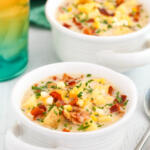 Potato corn chowder in a white soup crock with handles. There is a glass of ice water behind the bowl.