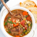 Beef barley soup recipe in white bowl sitting on white plate.