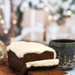 Gingerbread slices on wooden board with gingerbread loaf. There is a Christmas mug beside the board.