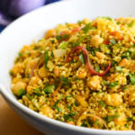 Bulgur wheat salad with chickpeas and red onion in a white bowl on a gold charger platter.