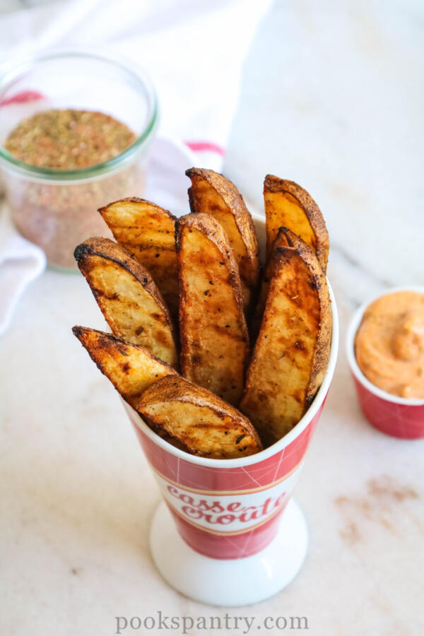 Grilled potato wedges with spice mixture and dipping sauce in background.