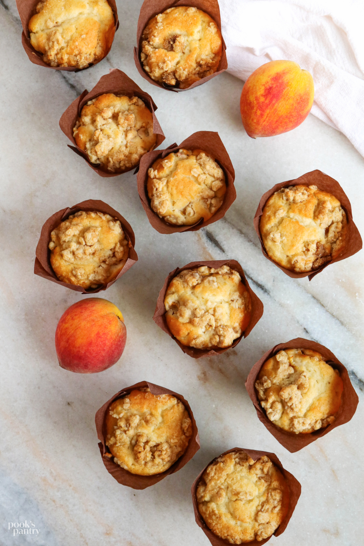 Peach crumble muffins on a marble cutting board with 2 whole peaches next to the muffins.