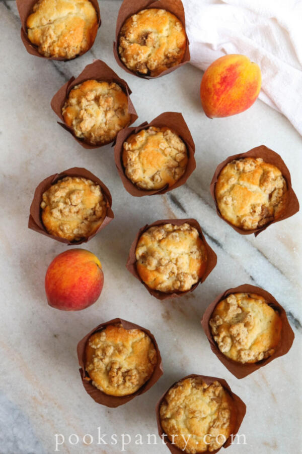 overhead view of peach muffins with crumble topping on marble board