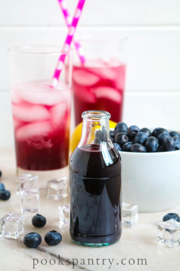blueberry simple syrup for cocktails with drinks in background and bowl of blueberries