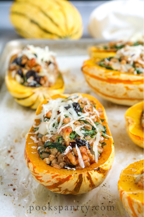 Stuffed delicata squash on sheet pan sprinkled with cheese.