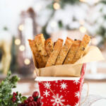 Almond biscotti in red and white treat box with brown parchment paper in from of a Christmas background.