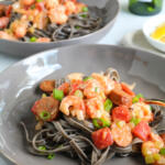 Cajun pasta with langostino tails and andouille over squid ink pasta in gray bowls.