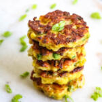Stacked curried cauliflower cakes on a white background with chopped scallions on the side.