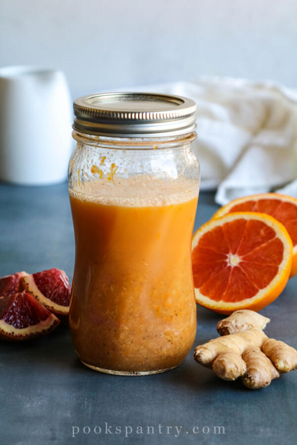 Orange ginger dressing in glass jar with oranges and ginger beside jar
