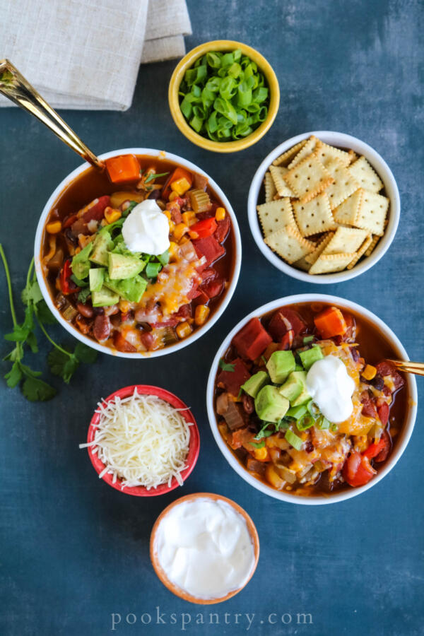 vegetarian chili in white bowls with herbs, sour cream and avocado
