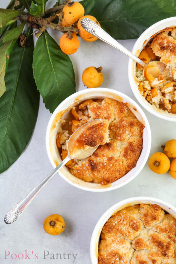 loquat cobbler in white baking dish with spoon