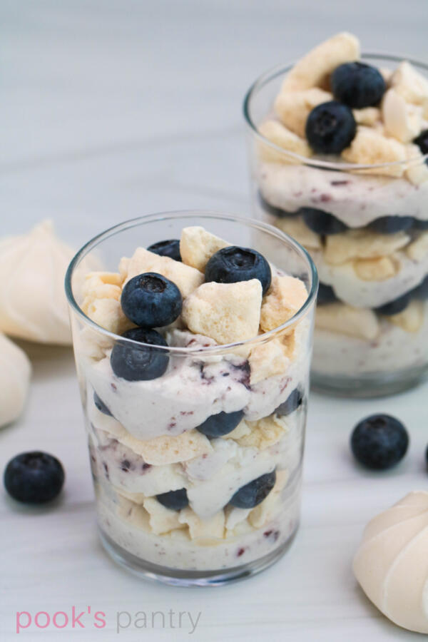 Eton mess with fresh blueberries and meringue cookies in clear straight sided glasses.