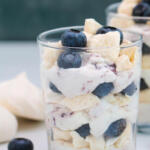 Blueberry Eton mess in clear glass with blueberries in the background.