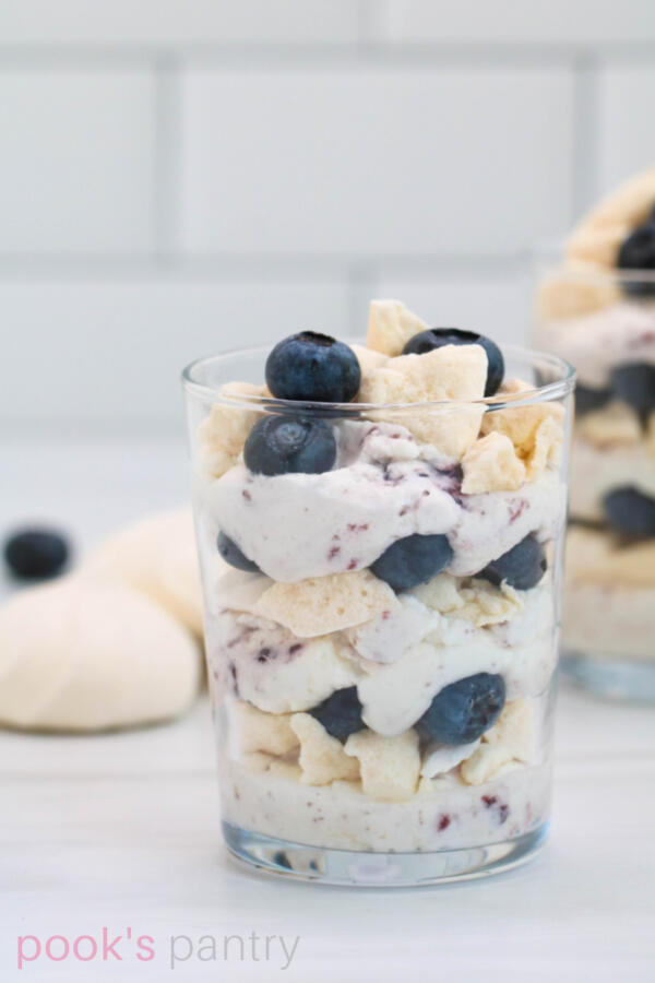 Blueberry Eton mess in small clear glasses with meringue cookies and blueberries in background.