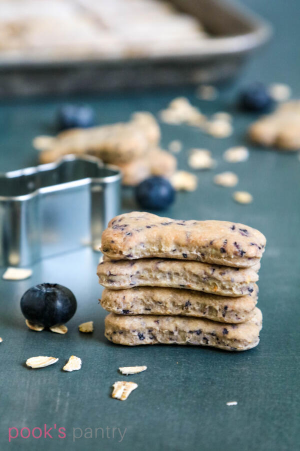 Four blueberry dog treats stacked on top of each other with one blueberry sitting on top of rolled oats.