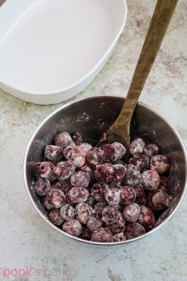 Cherries mixed with flour, sugar and lemon juice in stainless steel mixing bowl.