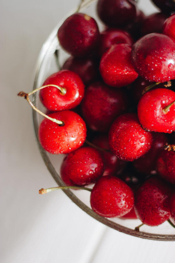 Red cherries in a glass bowl with a white background.
