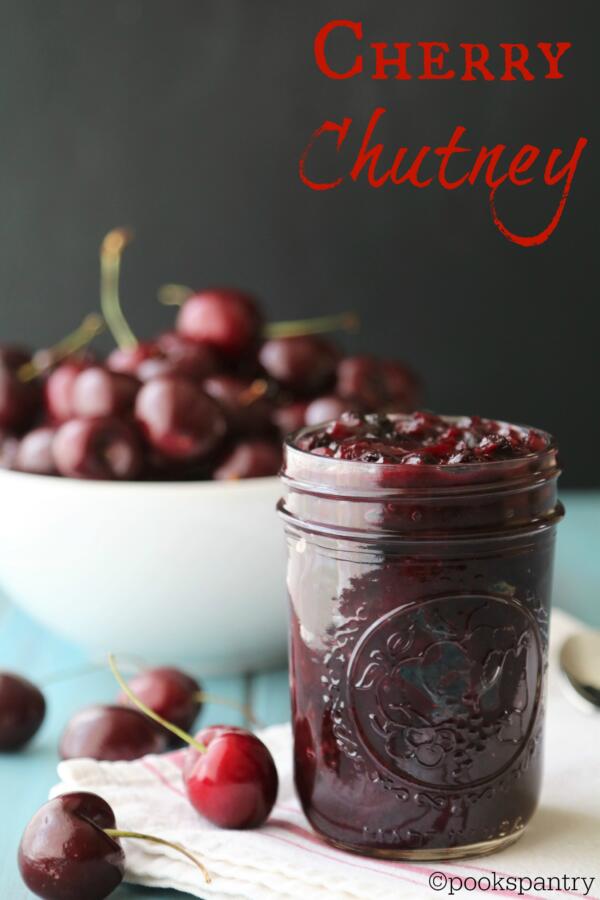 Cherry chutney in glass canning jar with a bowl of cherries in the background.