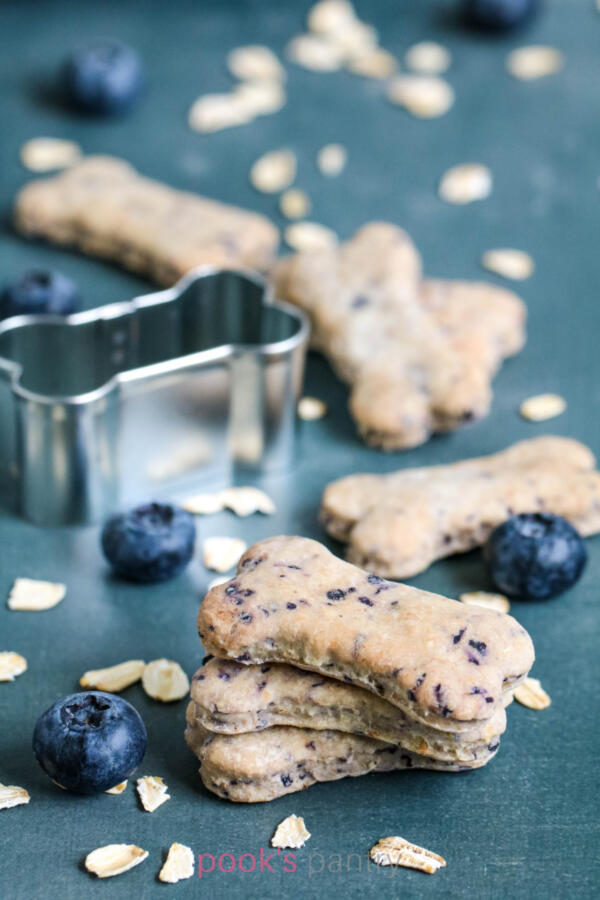 Stacked dog treats with blueberries with rolled oats sprinkled around them.