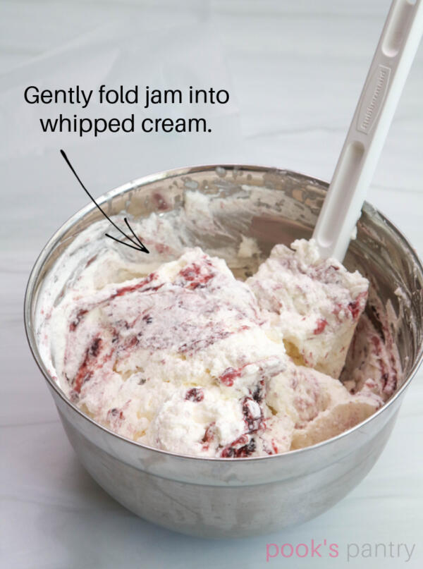 Mixing bowl full of whipped cream with jam folded into it for Eton mess recipe.