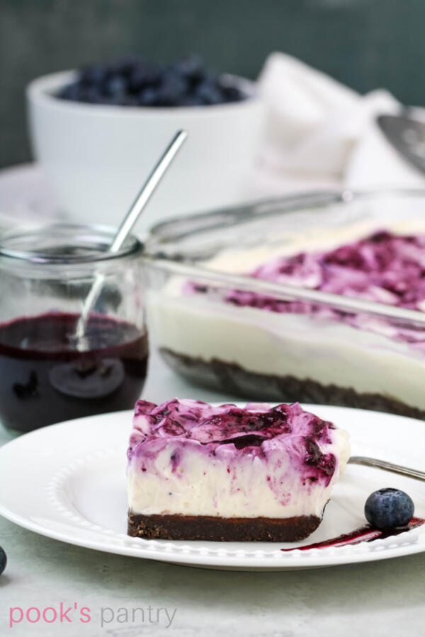 No bake blueberry cheesecake slice on white plate with blueberry and sauce.
