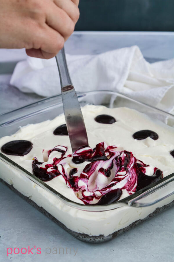 Swirling blueberry sauce into no bake cheesecake with butter knife.
