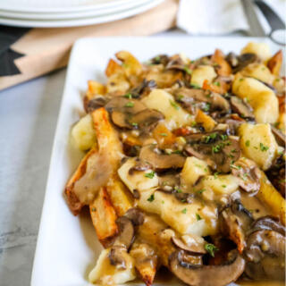 Vegetarian poutine with mushroom gravy on rectangular white plate.