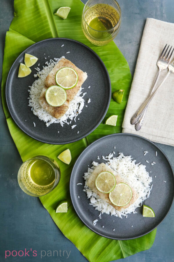 Plates of grilled corvina with limes on a banana leaf on gray background.