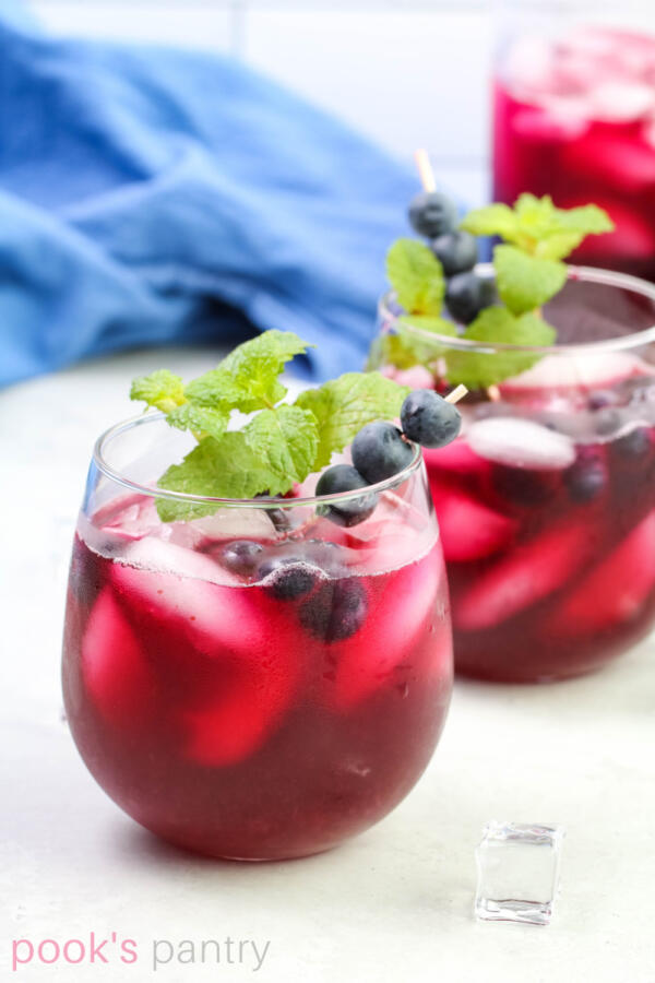 Blueberry lemonade recipe in clear round glasses with blueberries and mint garnish.