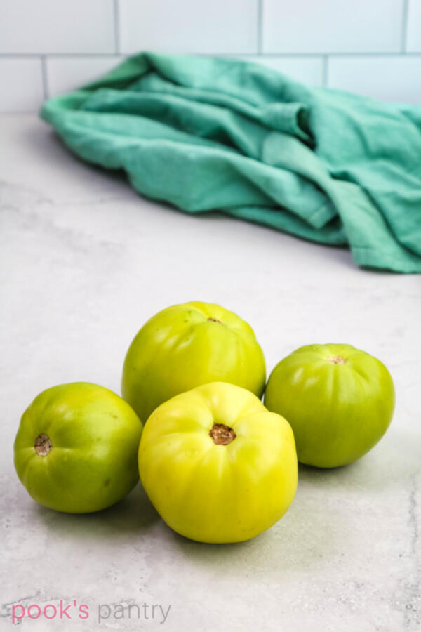 4 green tomatoes grouped together on a gray background.