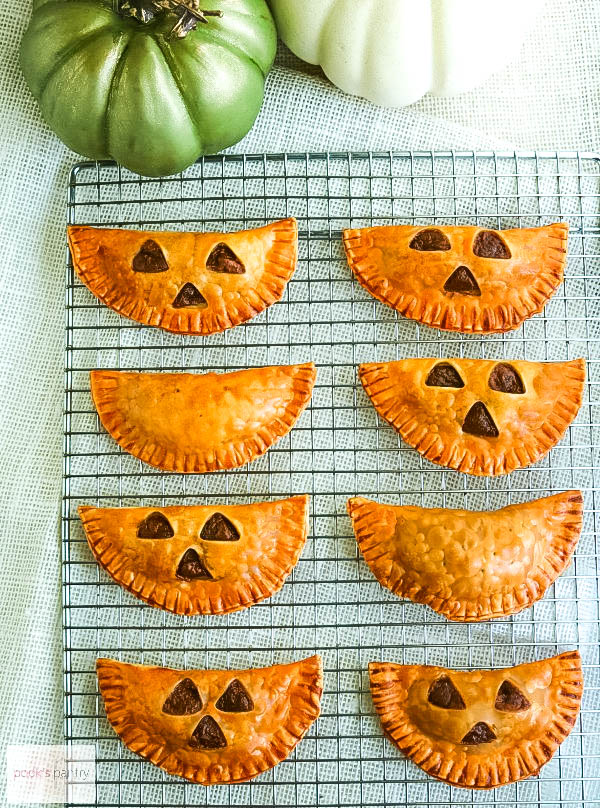 Empanadas filled with pumpkin on cooling rack. Empanadas have faces cut out of the dough to look like jack o' lanterns.